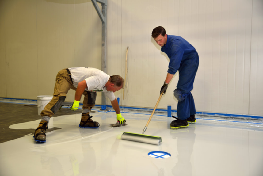 Dos empleados de Plancher Epoxy Granby aplican el epoxi al suelo con una paleta y un rodillo.